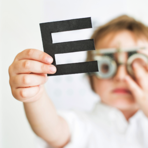 Dziecko w próbnej korekcji okularowej w gabinecie ortoptycznym trzymające w ręku literę E.